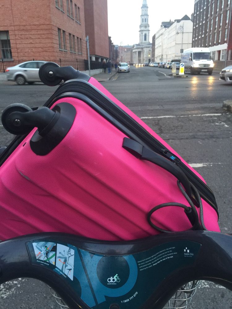 Pink suitcase in the basket of a Dublin Bikes bike share bicycle basket. 
