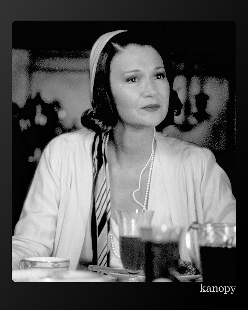 Black and white image of actor Carrie Fisher in a scene from the film, wearing headphones and sitting at a table with a drink.