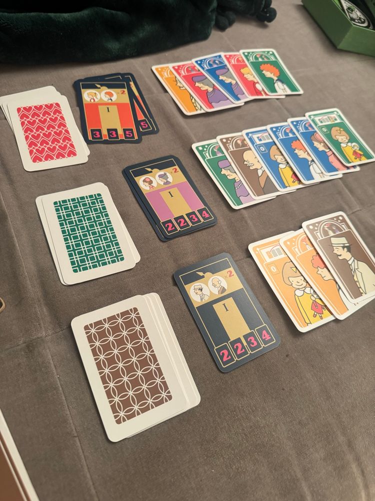 Cards from the game in front of an elevator splayed out with different colors (yellow red blue green and brown) lined up in front of elevator scoring cards 