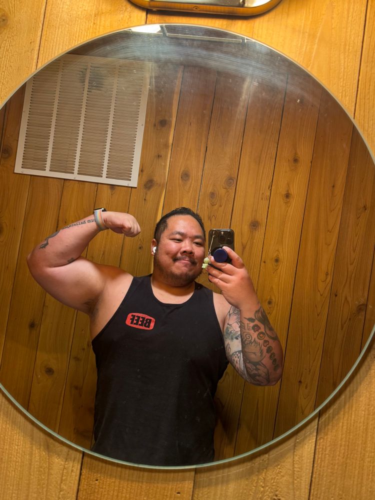 Danny flexing bicep in a circle mirror with a tank top that says beef