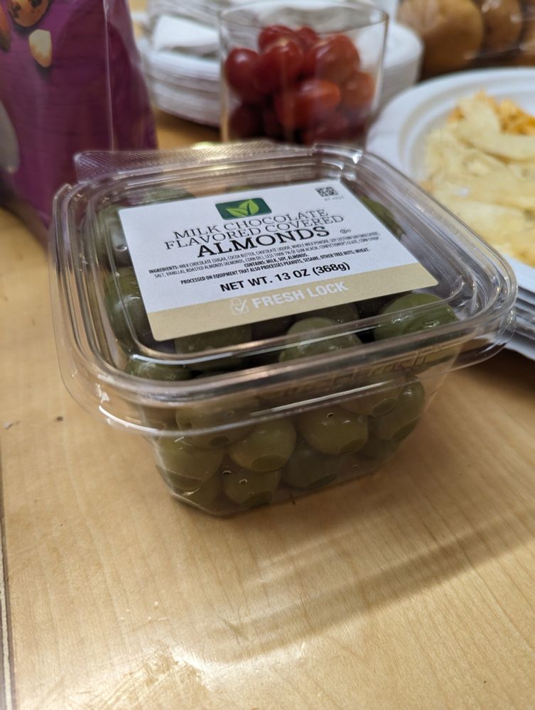 A clear container labeled as chocolate covered almonds that contains only a vile substance known as green olives.