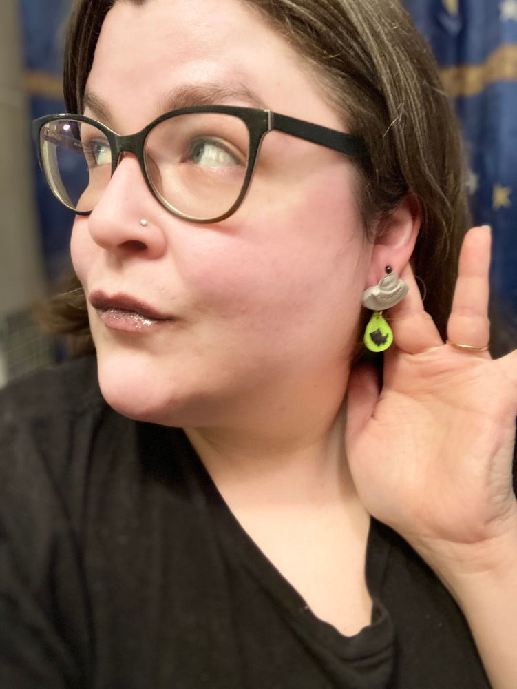 Ufo earrings incorporating a glass marble, and a neon teardrop shape showing a cat being abducted by the spacecraft, being worn by the artist.