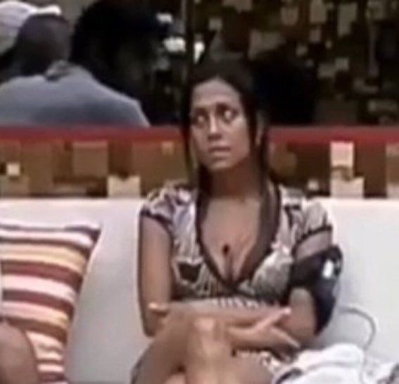 Lia do BBB sentada no sofá da sala de braços cruzados com um olhar de "quero te matar"