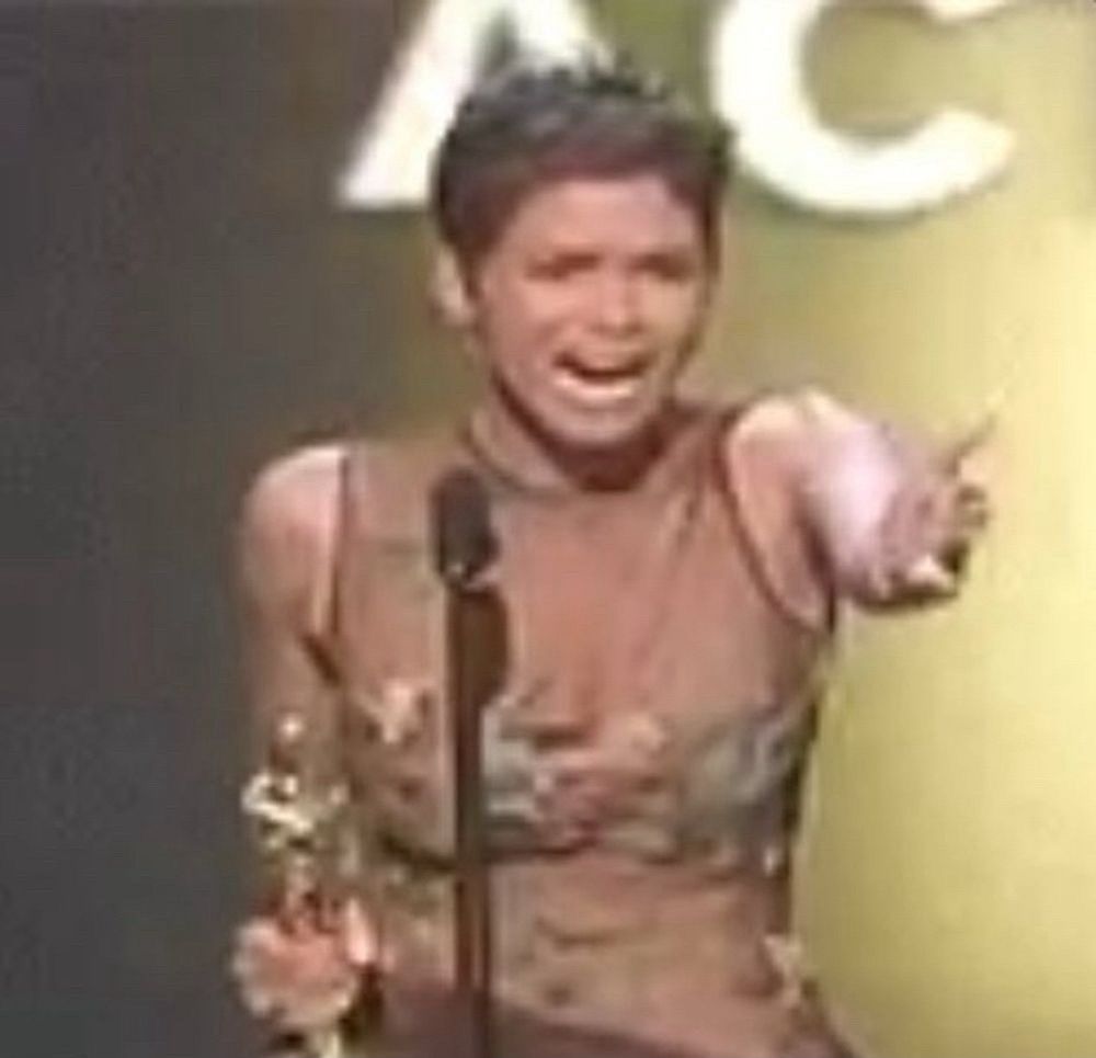 Halle Berry no Oscar com a estatueta na mão direita e com a mão direita esquerda apontando pra plateia com a boca aberta