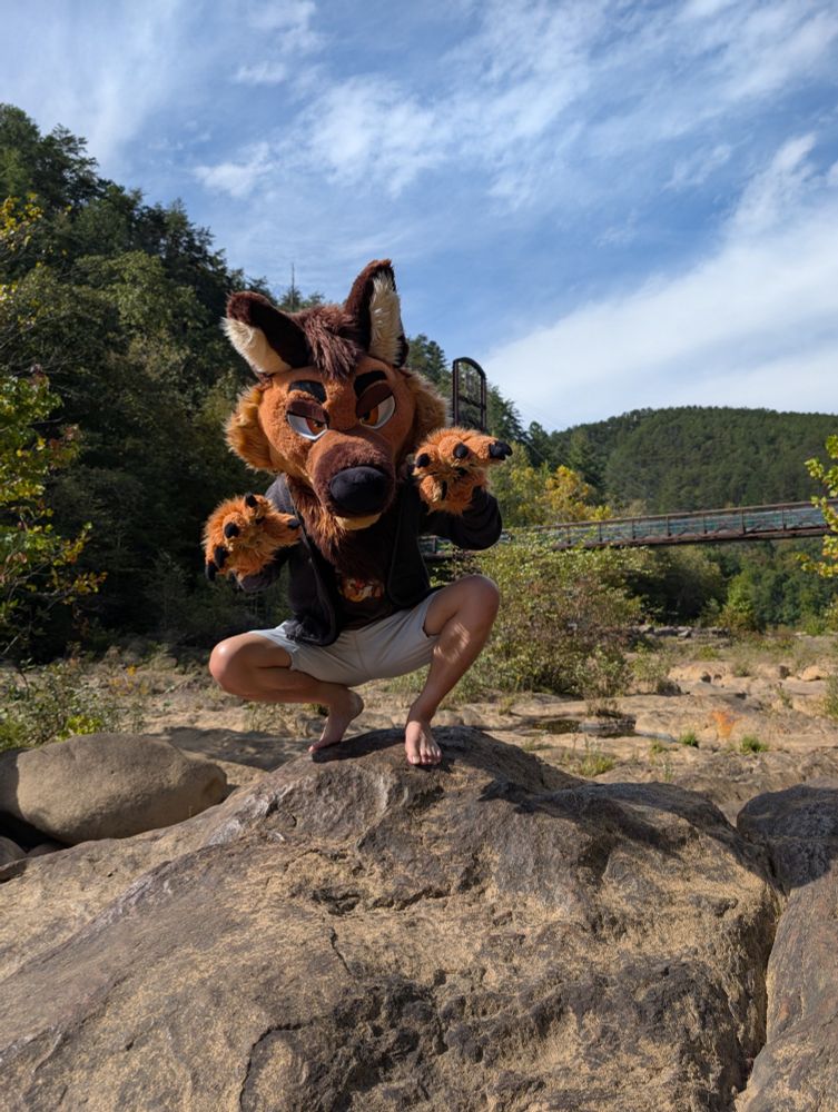 Trip is perched on a rock with his arms raised up, ready to pounce >:3c