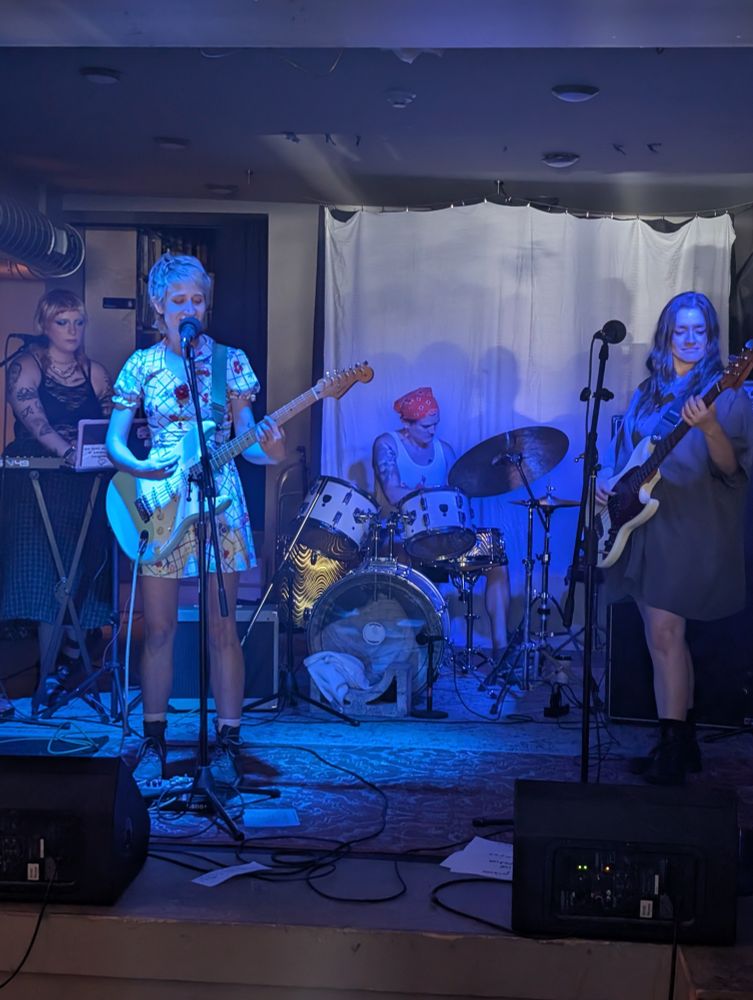 picture of petsitter on stage at the government center for the northside music festival. 4-piece band, guitar, keys, bass, and drums. we are all cutie-patooties. shout out to main street vintage, one of my fave vintage stores in this town, for the ridiculously cute dress that i (guitarist) am wearing in this pic. i recieved approx eleventy billion compliments and my ego will never recover