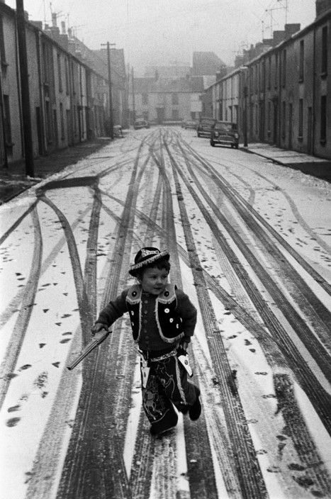 Street scene. 
View looking down a street, row of houses on both sides, snow on the ground, a small boy has a new Cowboy outfit on. 