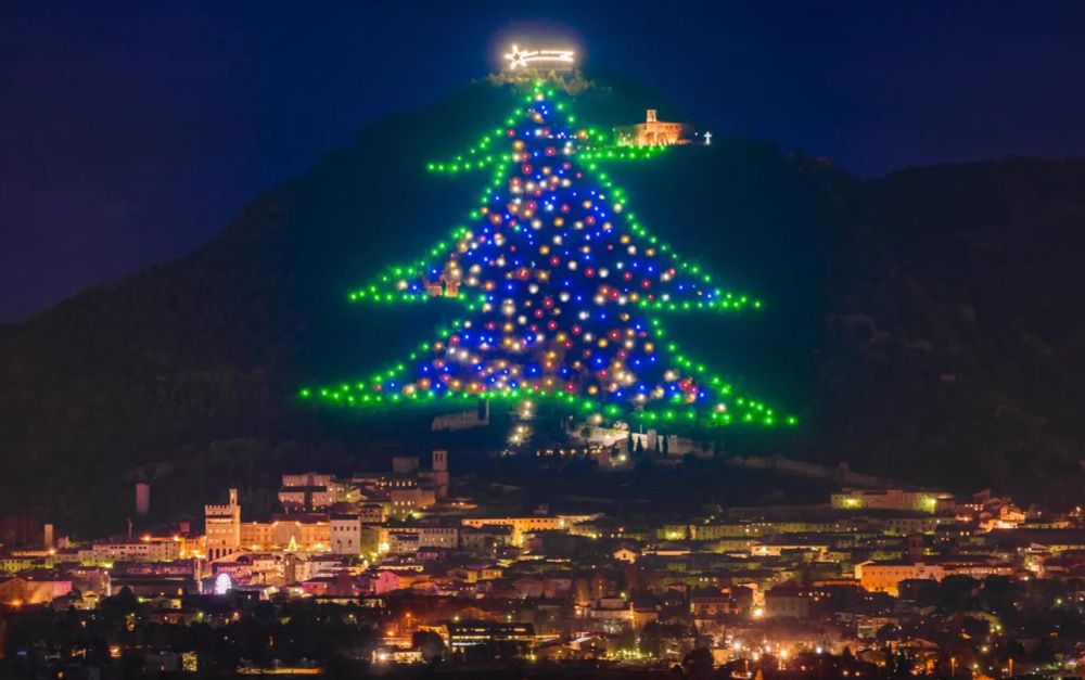 A Christmas tree made of huge lights going up the side of a mountain in Italy.  It looks like a kid's drawing of a Christmas tree.  Green lights outline, multiple color lights filling it in.