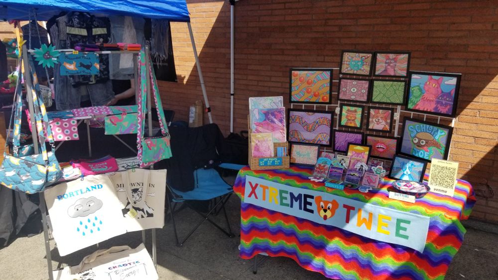 An art booth with brightly colored drawings, stickers, buttons, bags and more.