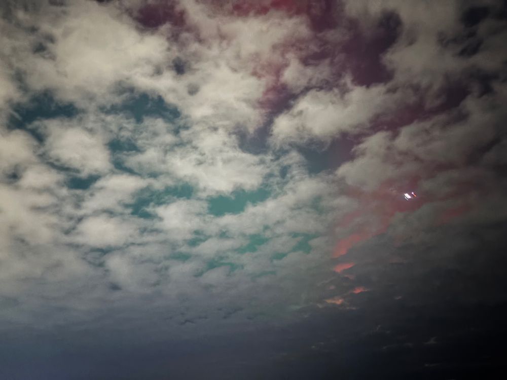 a photo of a night sky. Behind some clouds you can see (right to left) fuchsia and turquoise colors of the aurora borealis 