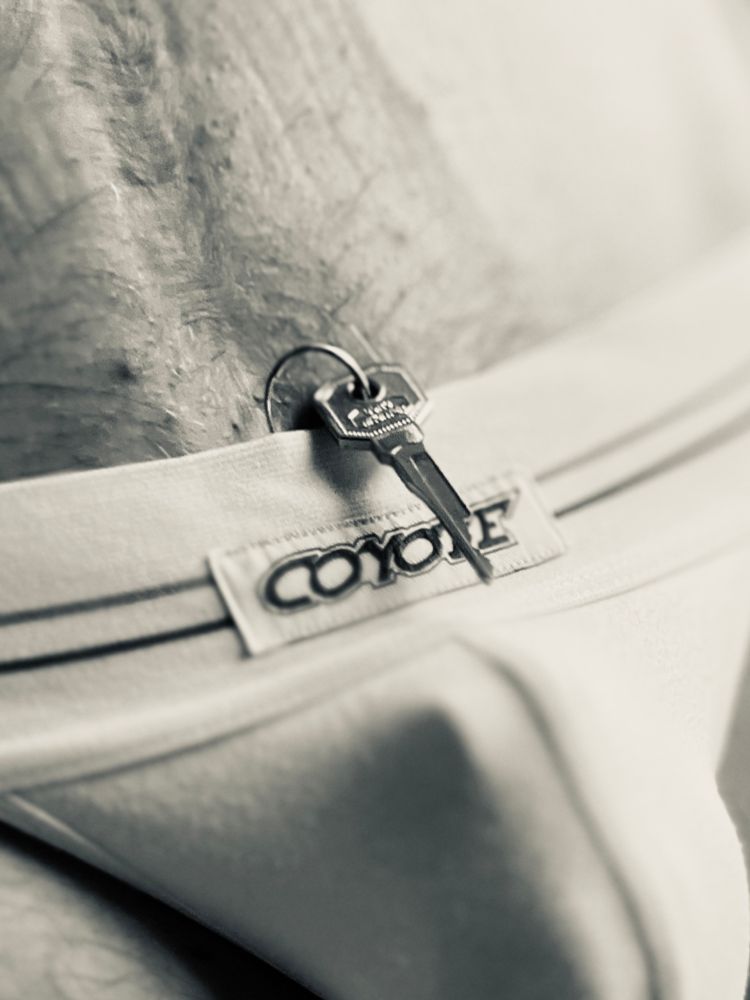 A very closeup black and white photo of the white waistband of a jock strap, with a key tucked into the front. 