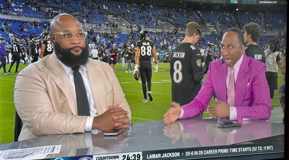 Steven A Smith wearing a light purple suit and going in about some dumb garbage like usual while another sportscaster tries to be calm and not look him in the eye.