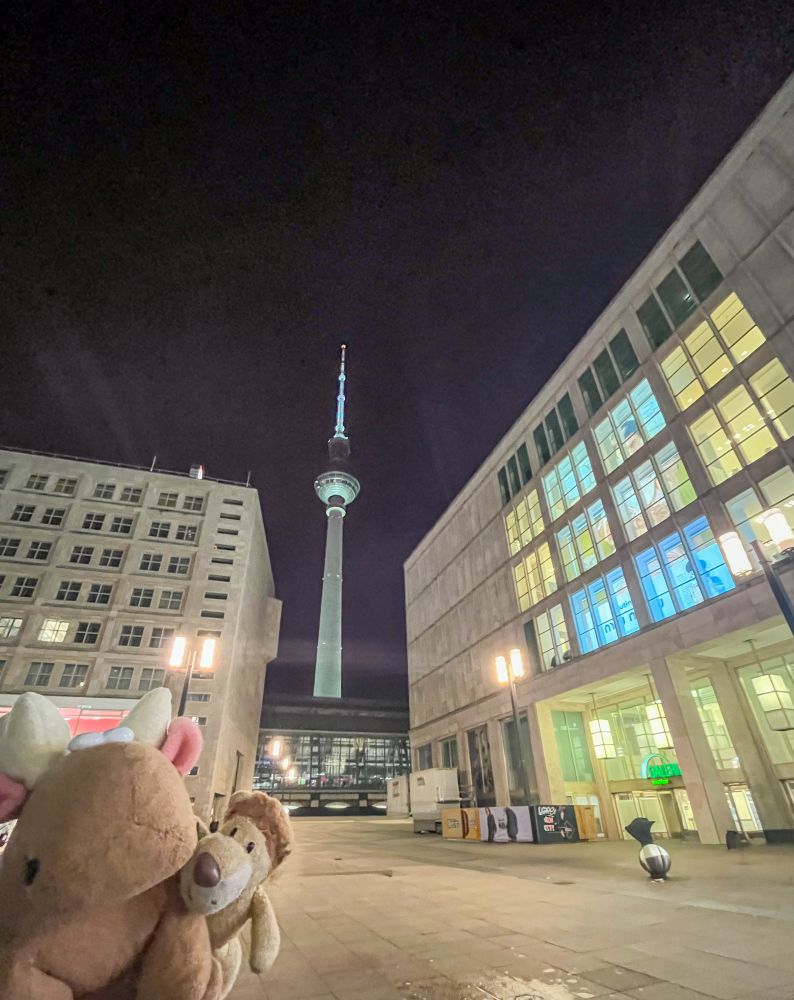 Röhrberto und Ludwig auf dem Alexanderplatz in der Dunkelheit. Der Fernsehturm ist hell erleuchtet.