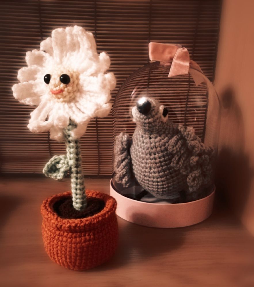 crocheted flower and in the background a crocheted bird under a glass dome