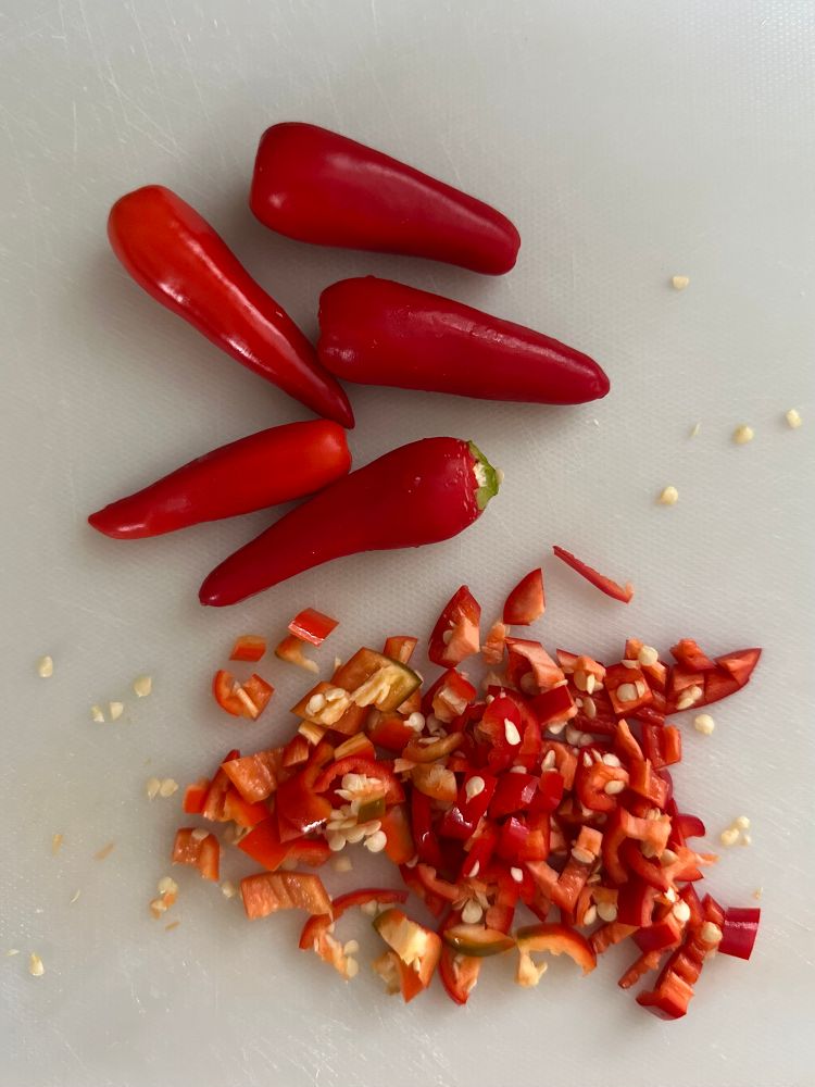 White cutting board with some whole Calabrian chile peppers and some chopped ones. 