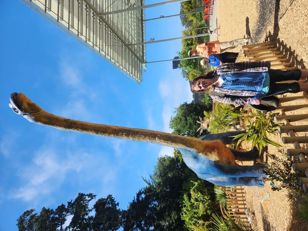Megan smiles and poses in front of an animatronic brachiosaurus