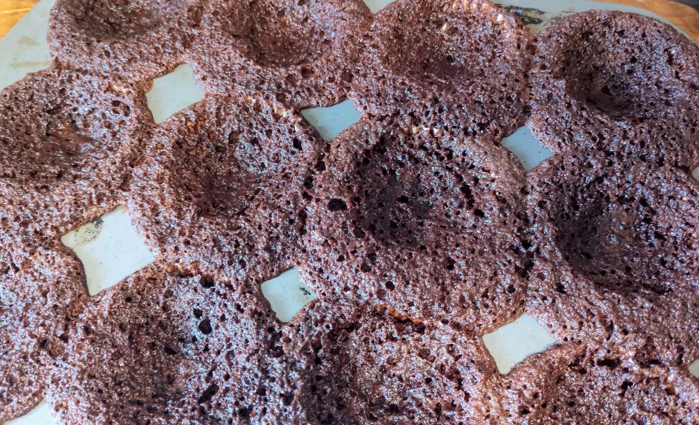 A tray of chocolate cupcakes that rose too quickly and then collapsed into craters overflowing their cups.