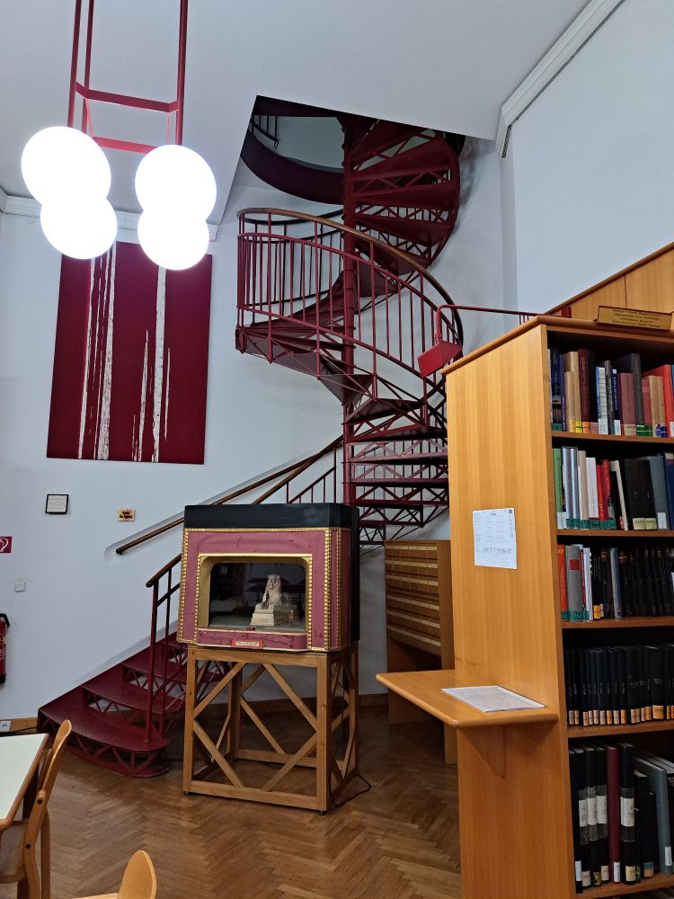 Blick auf eine Wendeltreppe und ein Ausstellungsobjekt in der Bibliothek von einem Arbeitsplatz aus.