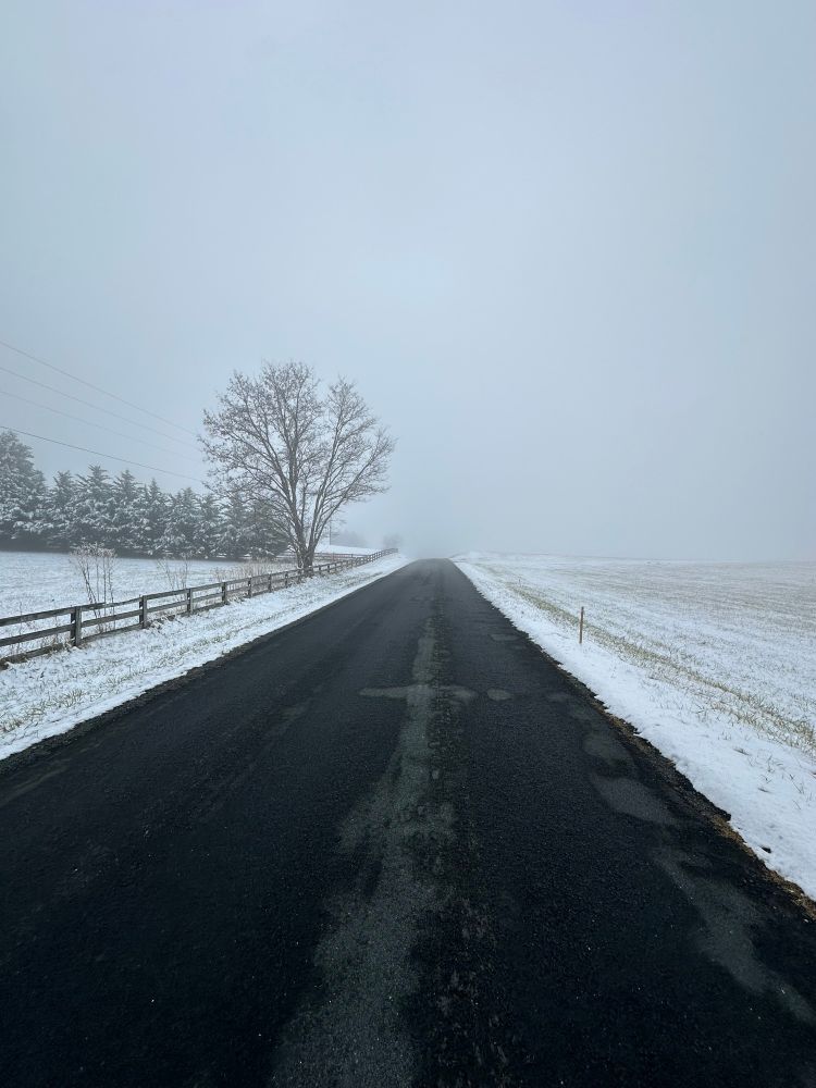 A country road outside of Amherst, VA.  Fields on both sides of the road are buried in snow, and the road appears to disappear in snowy mist in the distance.