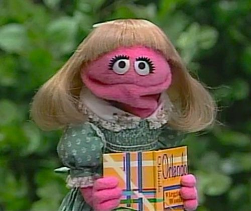 Prairie Dawn, a tiny hot pink Muppet with blonde hair and a blue dress, reading Orlando by Virginia Wolfe.
