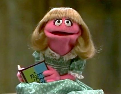 Prairie Dawn, a tiny hot pink Muppet with blonde hair and a blue dress, reading A Room Of Ones Own by Virginia Wolfe.