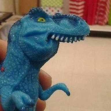 Tiranossauro Rex de plástico, de brinquedo, azul, mordendo o lábio inferior. Do meme “finofauro”. 