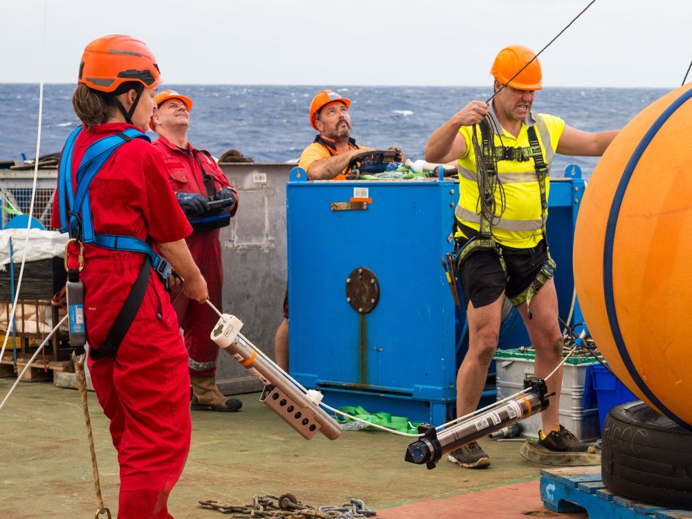 A ships crew are working together to lower a float, with multiple sensors attached, into the ocean.