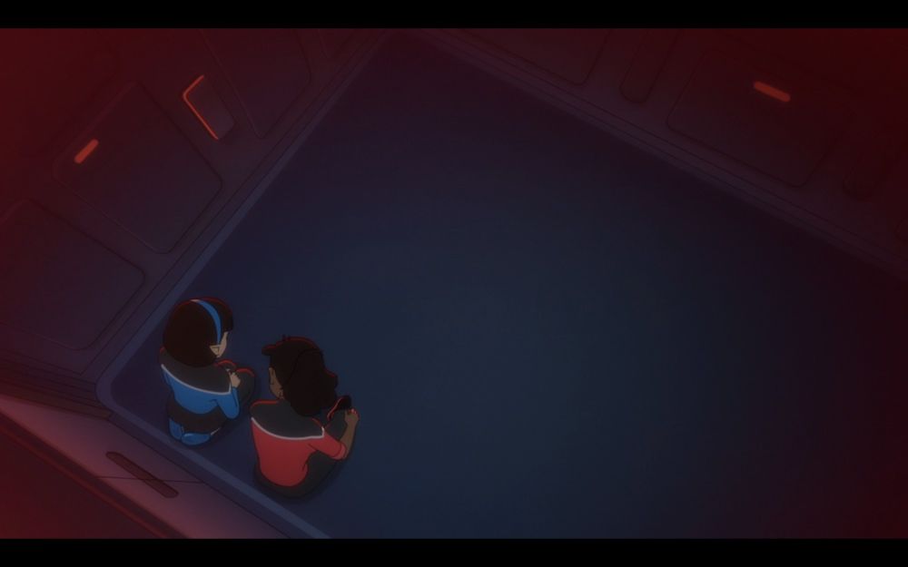 Two characters from Star Trek Lower Decks rest in a room on the starship Cerritos: T'Lyn, a Vulcan woman wearing the blue Starfleet uniform and a blue headband, kneels in the corner and confides that she does not feel "Vulcan enough" to Mariner, a Black woman with her signature ponytail wearing a red Starfleet uniform, who sits to her right.  The shot is framed with a Dutch Angle, and the characters are in the lower left corner, leaving the viewer to sense the negative space of the room (both intimate and oppressive) and its impact on the tangibility of the emotional moment.