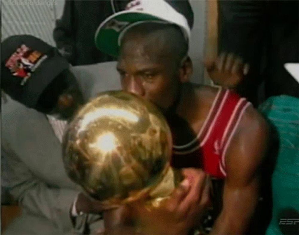 a man in a red and white jersey is kissing a gold trophy