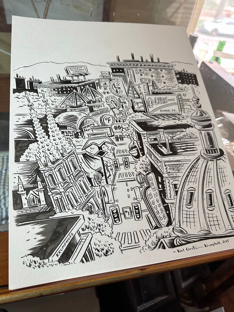 An inked illustration of East Colfax Avenue, Denver, CO sitting on a drawing table. 