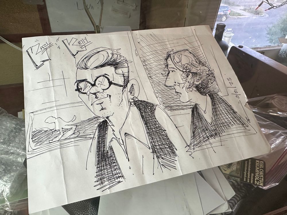 A caricature of Kelly and Karl sitting on a drawing table. 