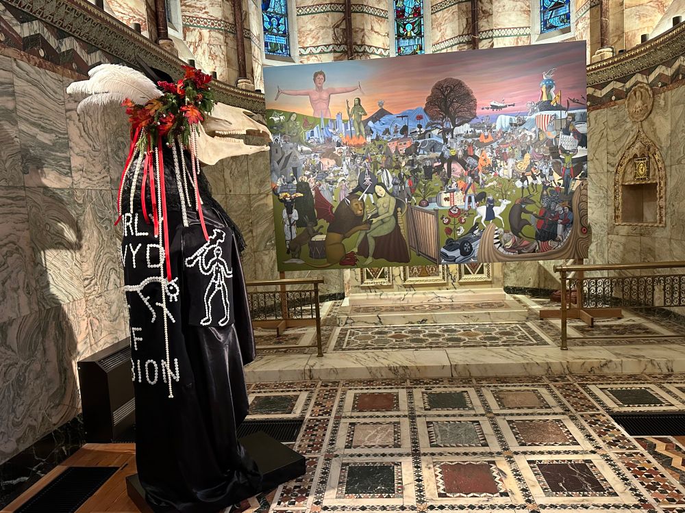 A mari lwyd sculpture in front of a large painting by Ben Edge in a chapel. 