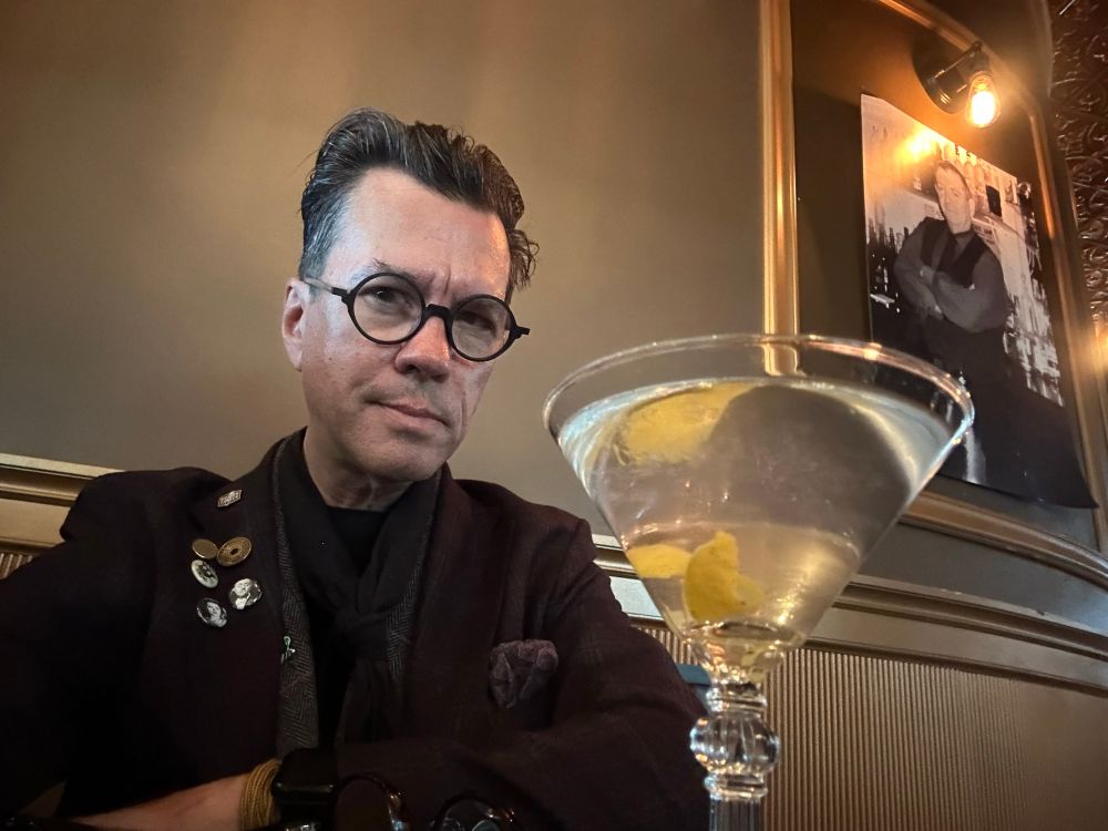 A man with glasses sitting with a cocktail