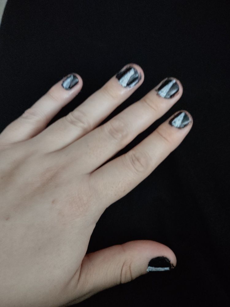 A picture of a hand over a black dress cloth. The nails are painted with black polish, and claws are painted over that black polish, from bottom to tip, suggesting a creature within.