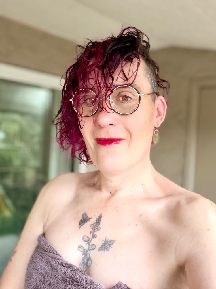 Siân, a white trans girl-ish, on nhw balcony wrapped in a towel, sharp shoulder bones distinct on pale skin.