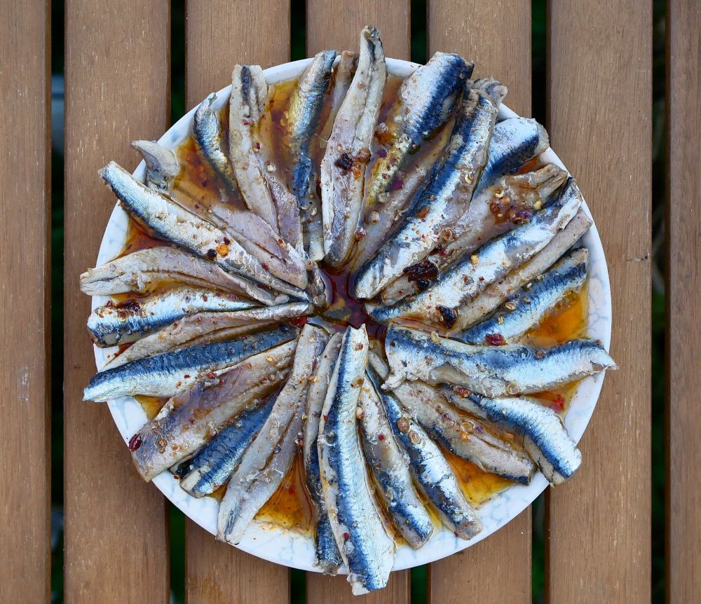 Top view of filets of fatty fish in orange red sauce on a dish, placed on a wooden table 