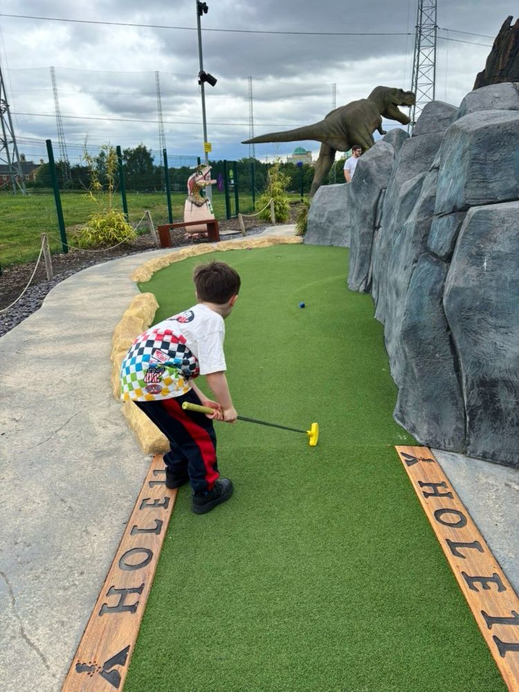 a little boy putting at a dinosaur mini golf course