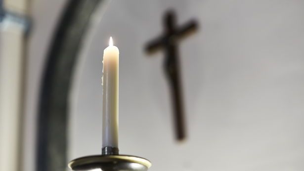 Lit candle, blurred crucifix on wall in background - Chapel of Thomas Guy