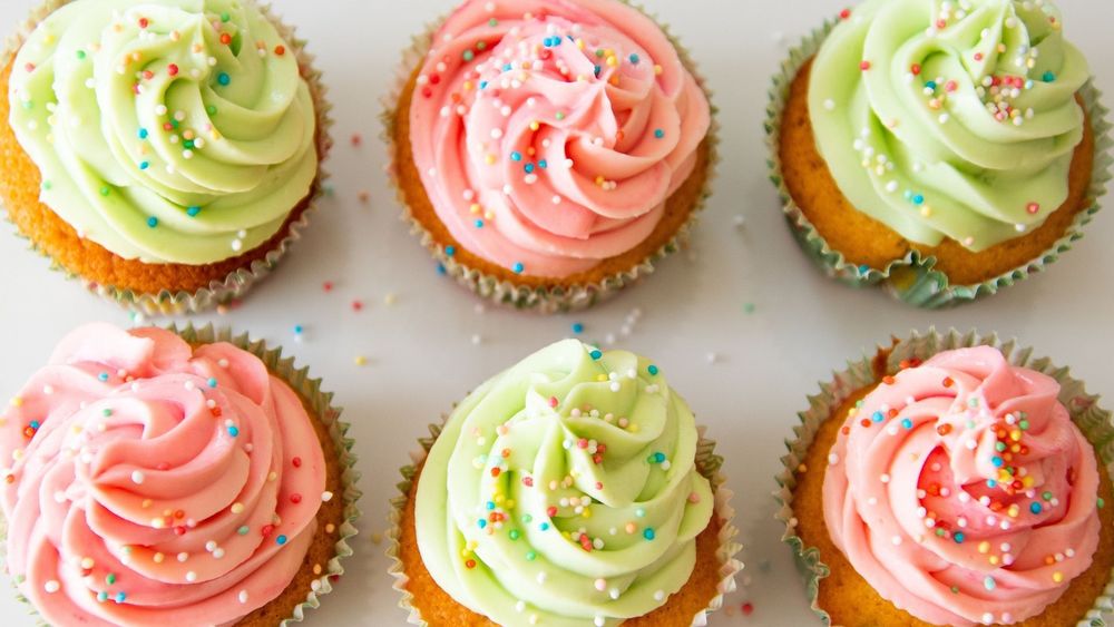 Pink and light green iced cupcakes with colourful sprinkles