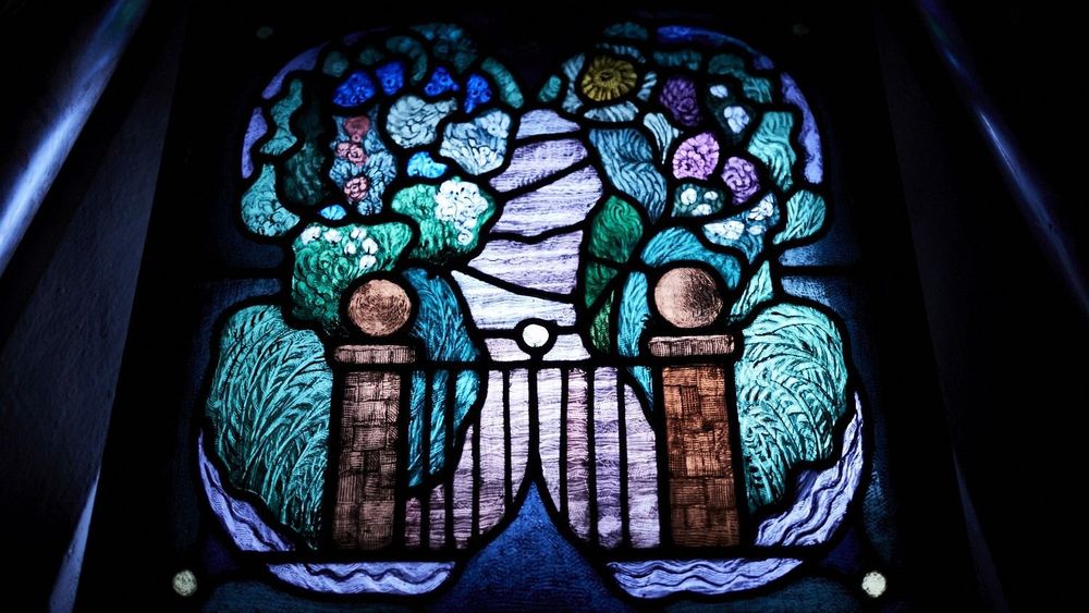 Stained glass window featuring a garden gate and path with foliage on either side - College Chapel, Strand