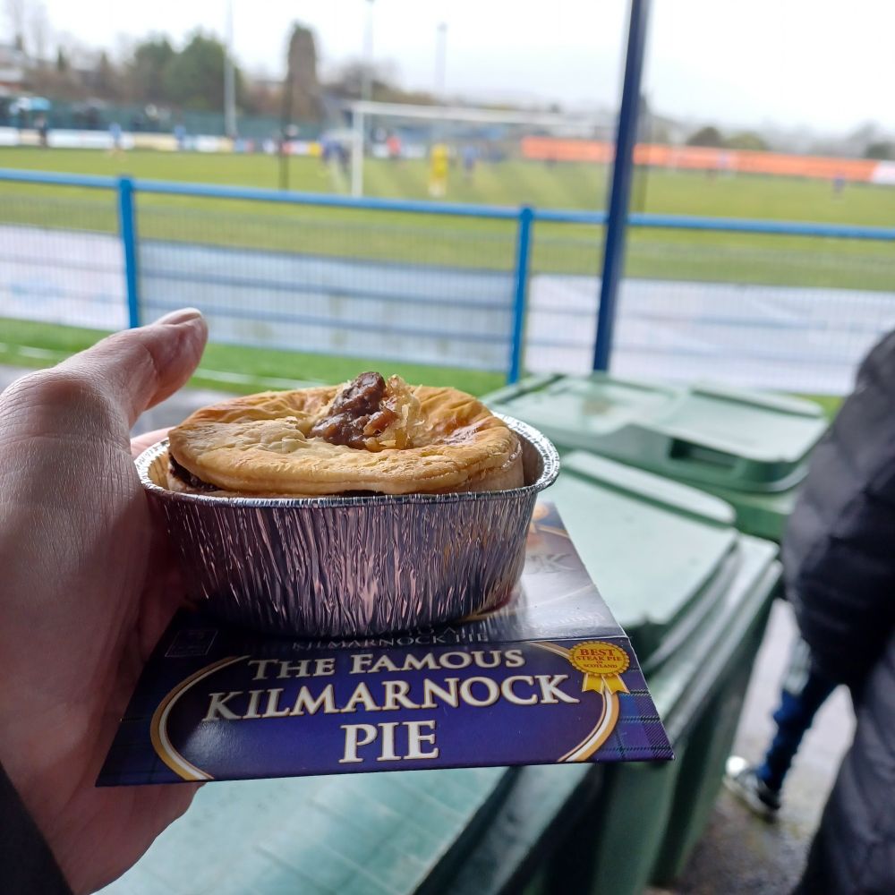 Pictute focused on a Killie (Kilmarnock) pie , with Darvel FC v Cumnock playing in background.
