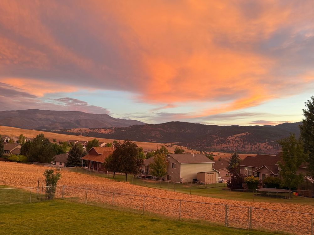 Peach and gray clouds above a strip of blue sky, mountains in the background, and golden light over a neighborhood. 