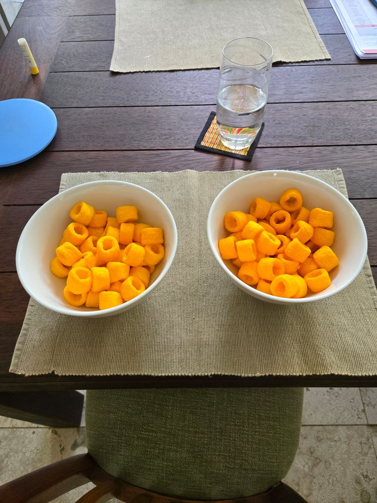 2 white bowls full of orange cheezles on a wooden table