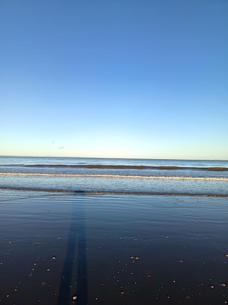 Waves gently breaking across a shoreline, the sand reflecting the dusty blues