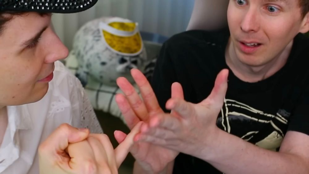 dan howell holding out his pinkie to phil lester who is holding it between his straightened fingers on both hands