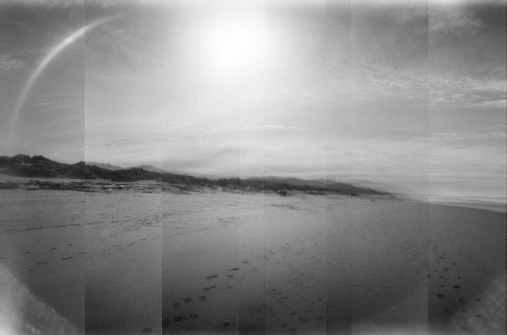 Black and white multiple exposure panoramic image of hills looking south from the sand on Manzanita Beach, Oregon. 