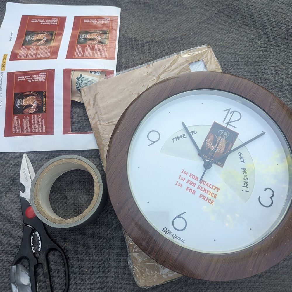 Fake wood round clock with picture of a ferret dressed like Henry VIII and the words 'time to get frisky!' hand written in Sharpie. Scissors and duct tape are next to it.