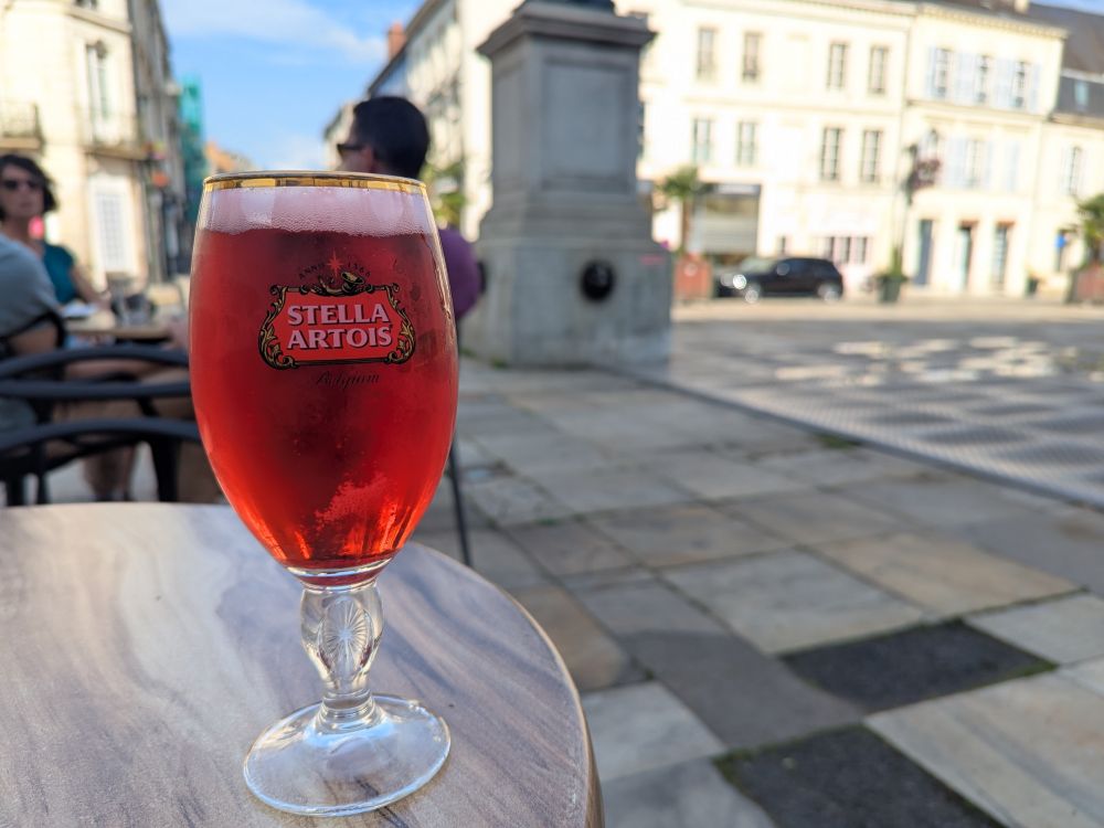 A beer glass with red liquid in it, sitting on a table overlooking a square.