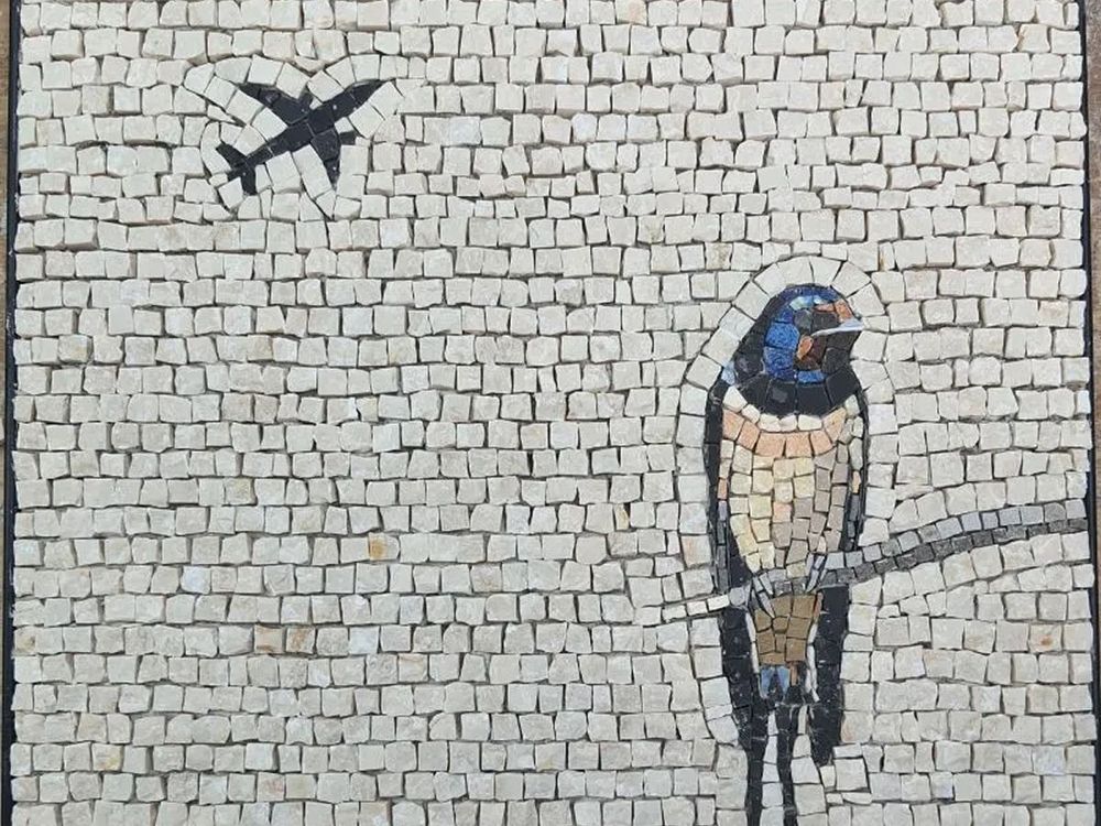 A mosaic showing, on the lower right a bird sitting on a branch. We think it might be a swallow. Top left, flying overhead is an aeroplane. 