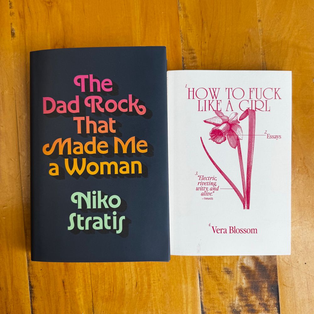 two books on a wooden table: The Dad Rock That Made Me a Woman by Niko Stratis, and How To Fuck Like A Girl by Vera Blossom